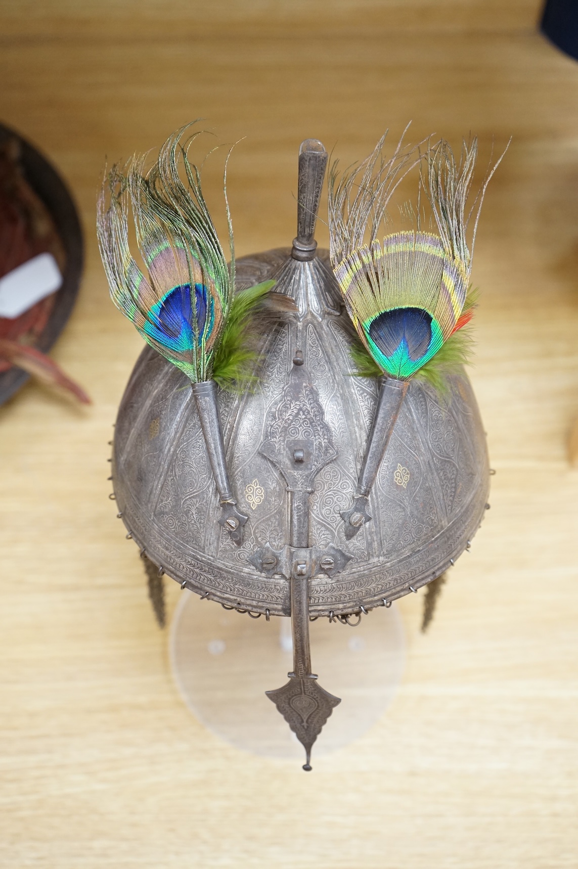 A mid to late 19th century Indian helmet and matching shield, covered with silver koftgari decoration, the helmet with sliding nasal bar and twin plume sockets surmounted by a third plume socket, the skull fluted like a